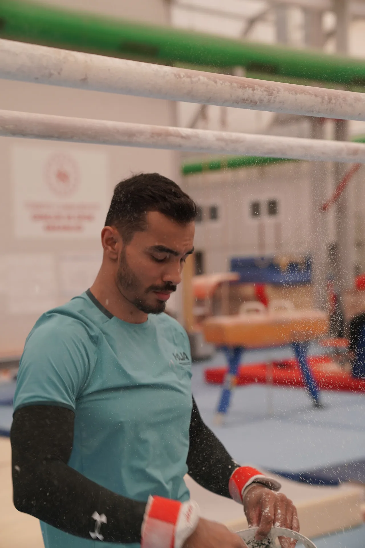 Ferhat Arıcan applying chalk to his hands in a gymnastics hall