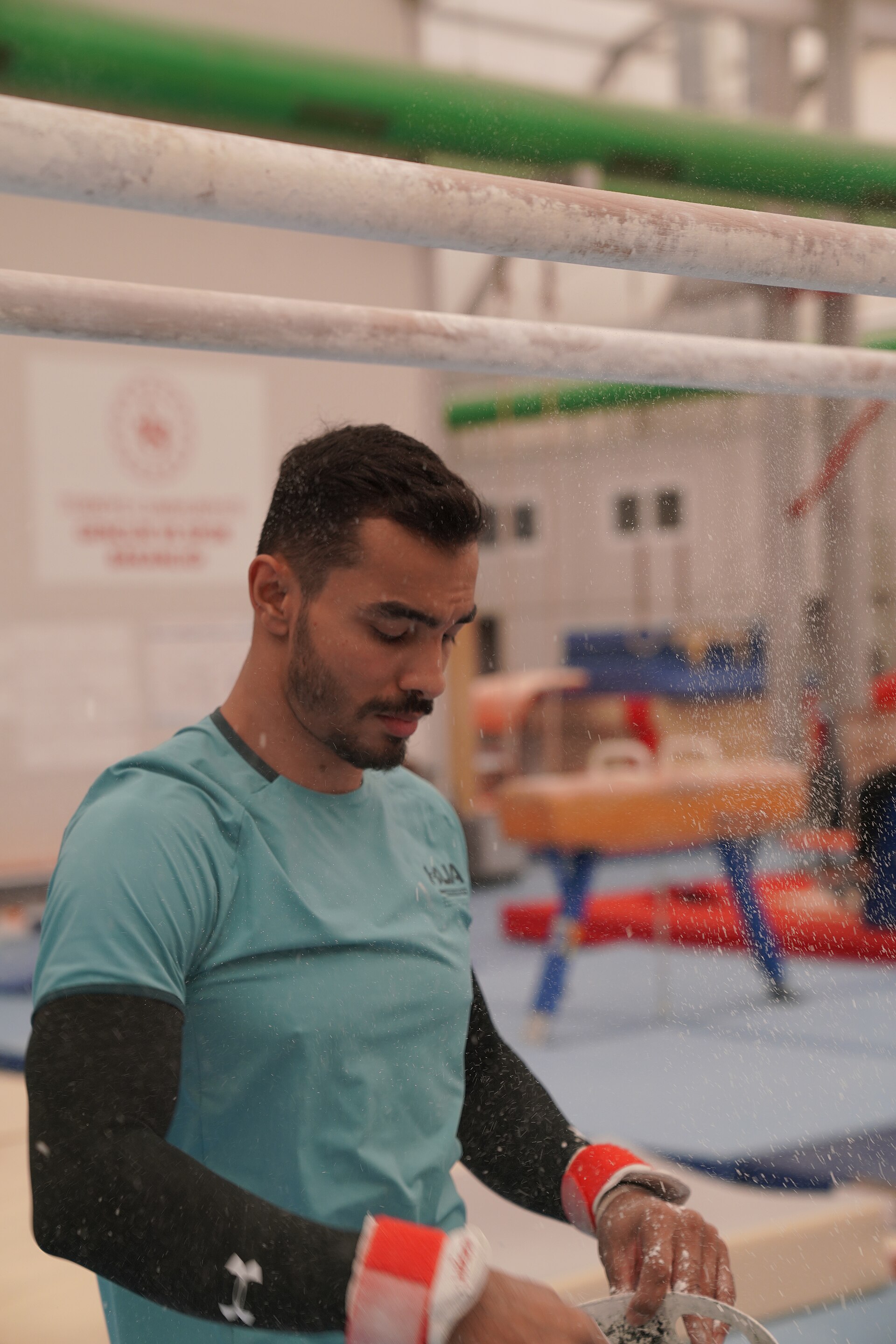 Ferhat Arıcan applying chalk to his hands in a gymnastics hall