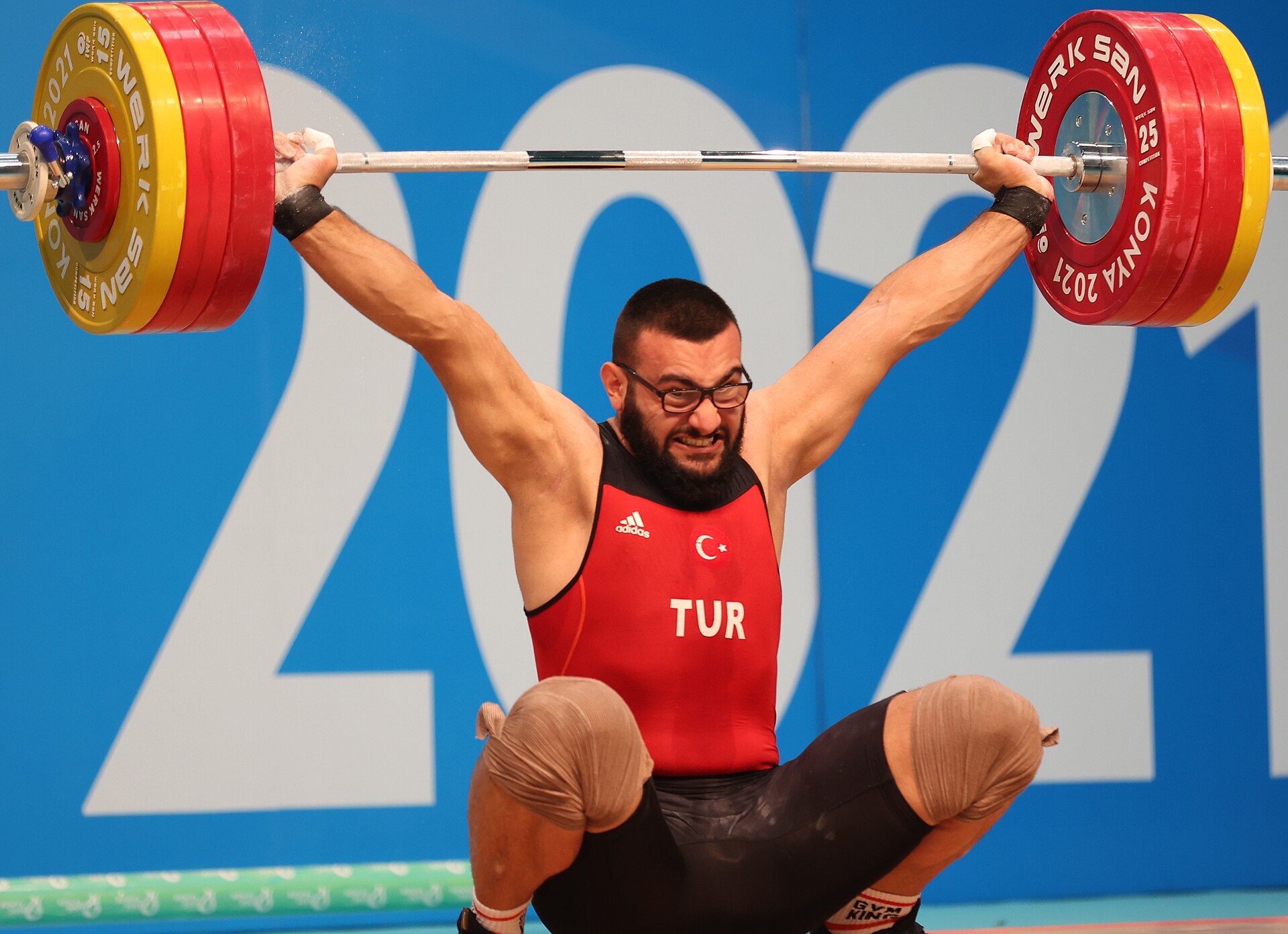 A weightlifter in Türkiye colours stabilises the bar overhead in the snatch