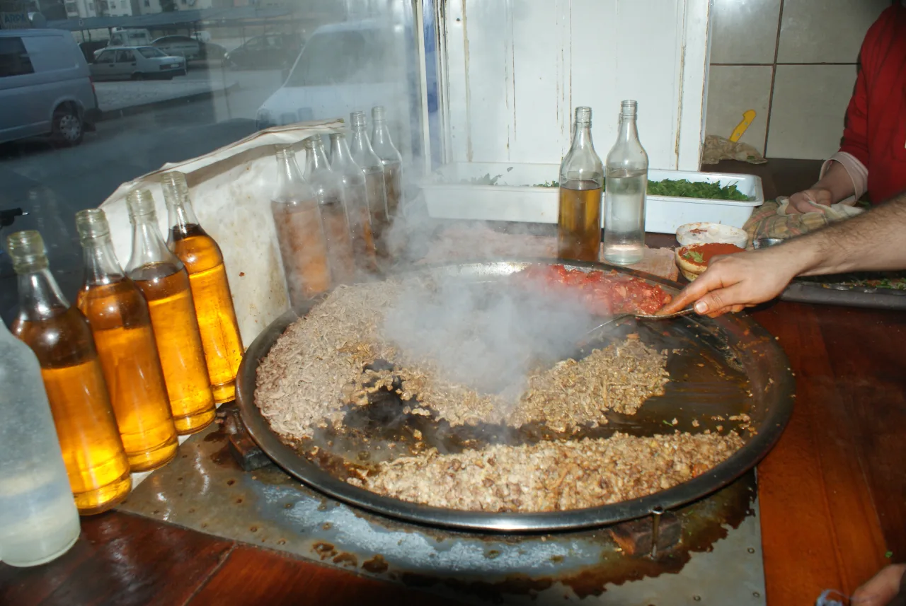 Hands preparing tantuni in a wide metal pan, with meat and steam
